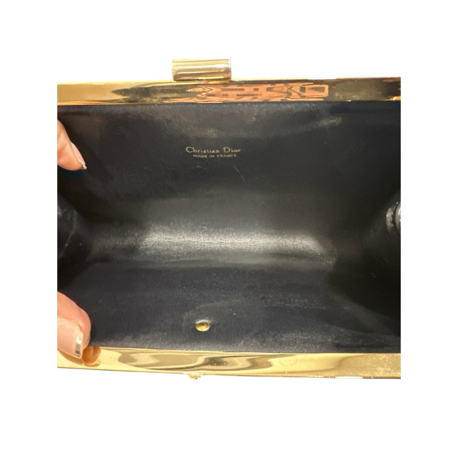 Black clutch bag with gold frame and Christian Dior branding on a white background