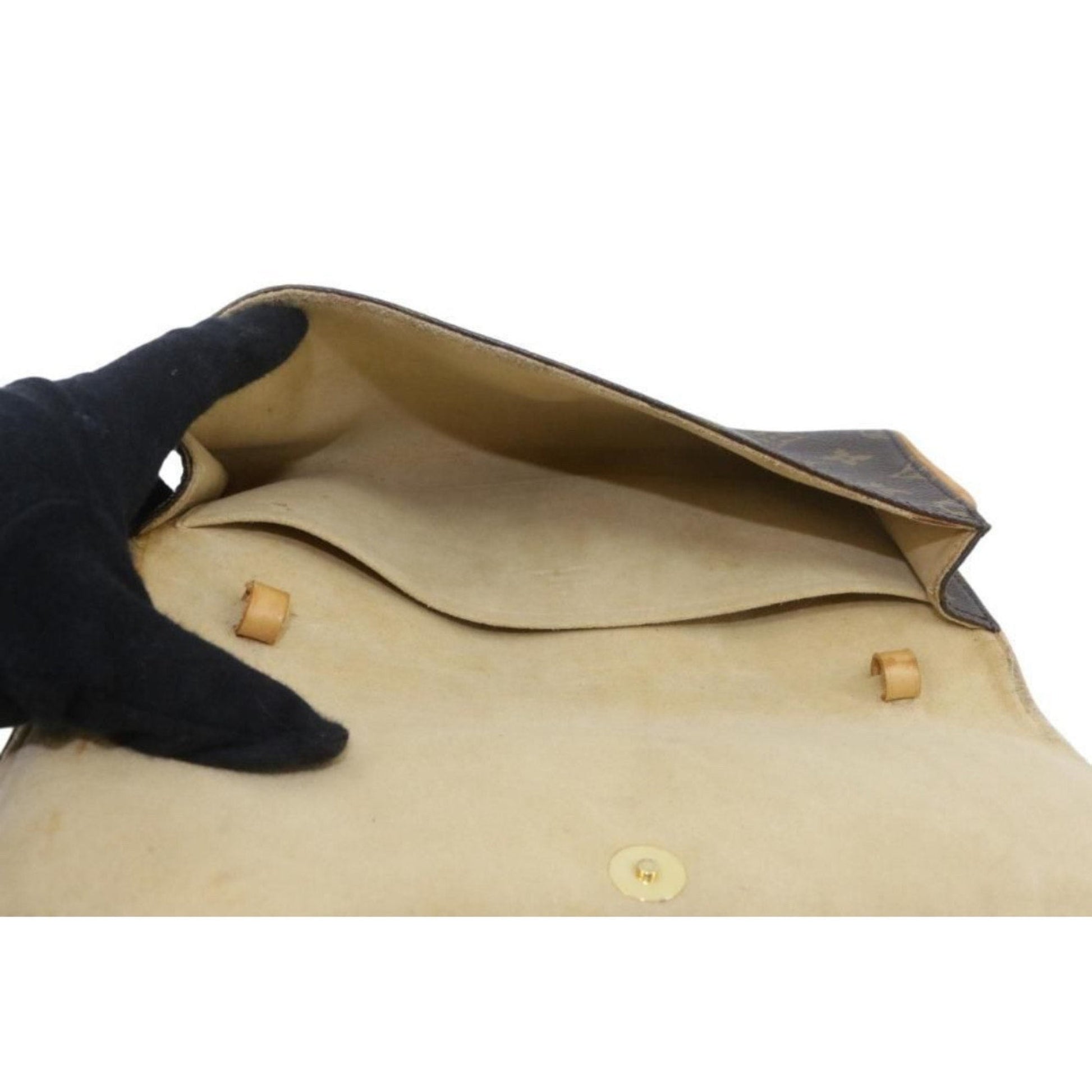 Close-up of a beige leather bag with wooden buttons, held by a black-gloved hand on a white background.