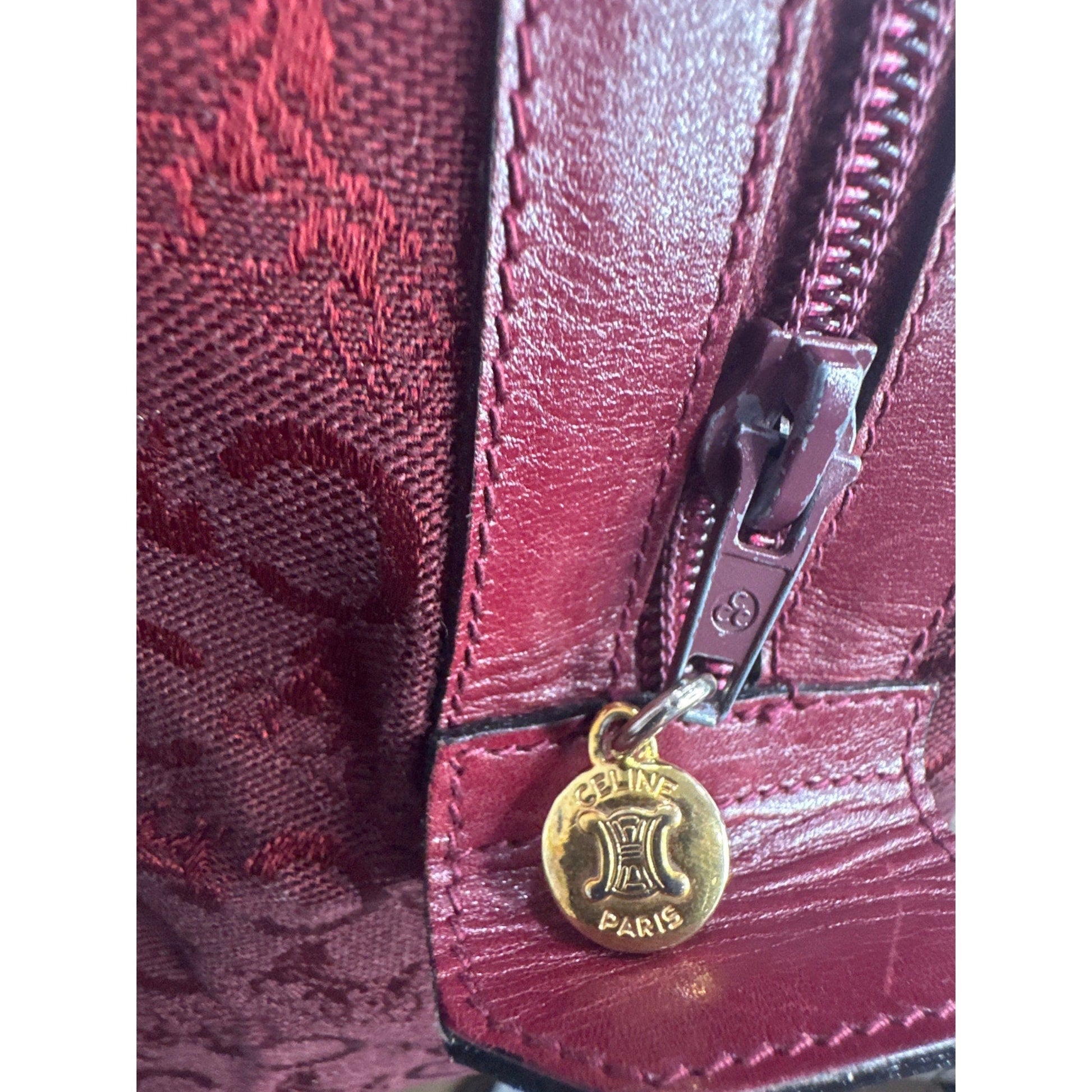 Close-up of a red textured bag with a gold tag featuring a logo.