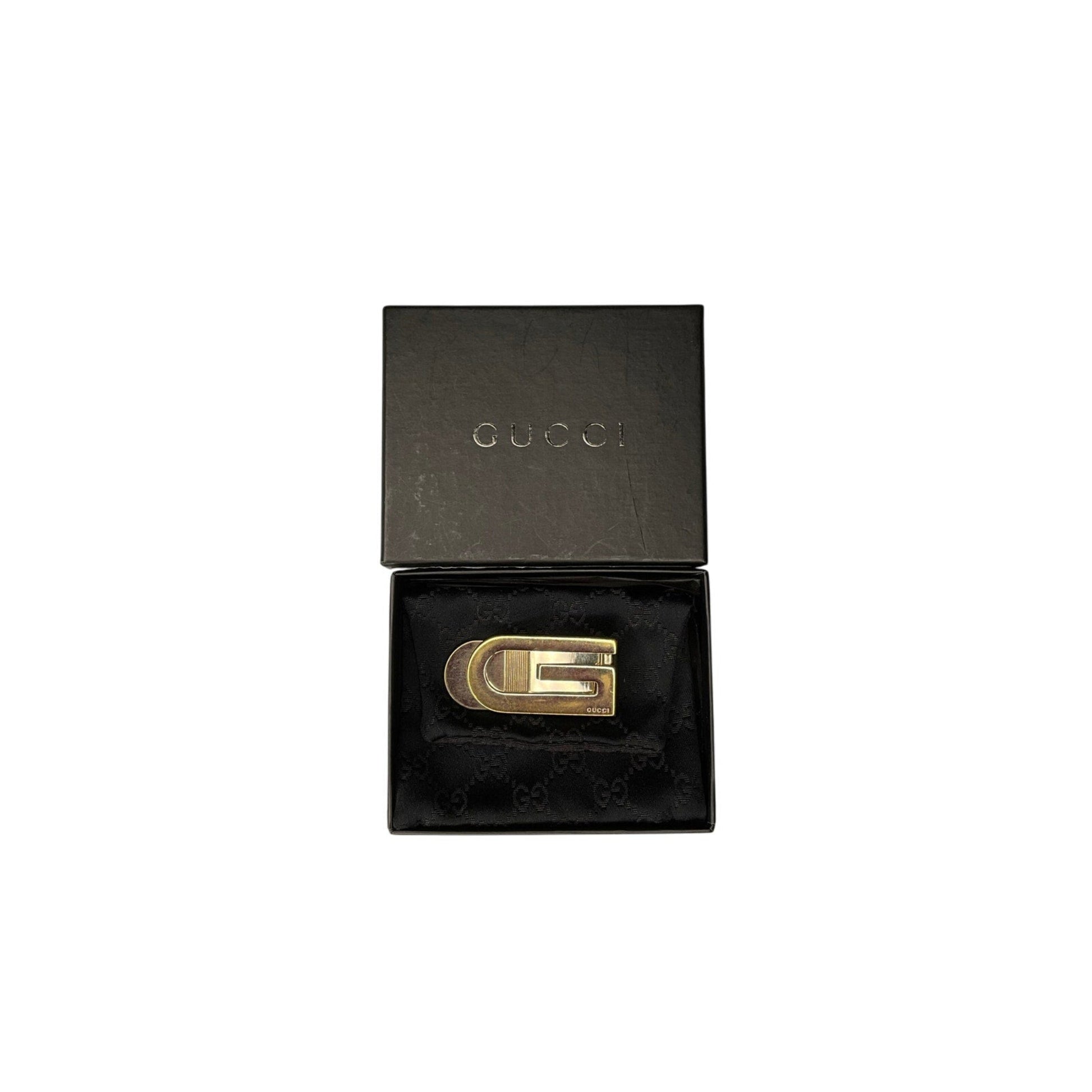 Gold Gucci belt buckle in a black box on a white background