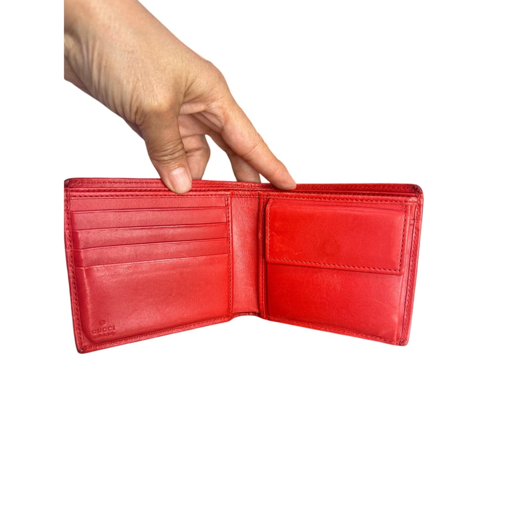 Red leather wallet held open by a hand on a white background