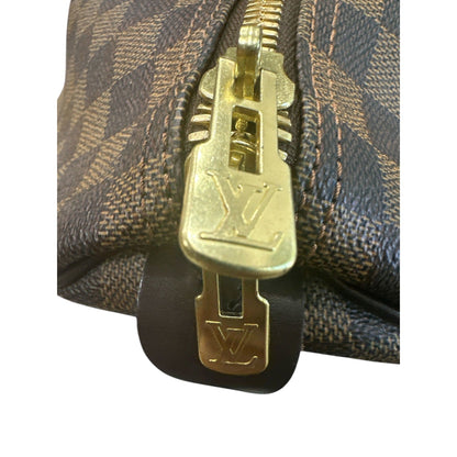 Close-up of a gold zipper pull on a Louis Vuitton bag with monogram pattern.
