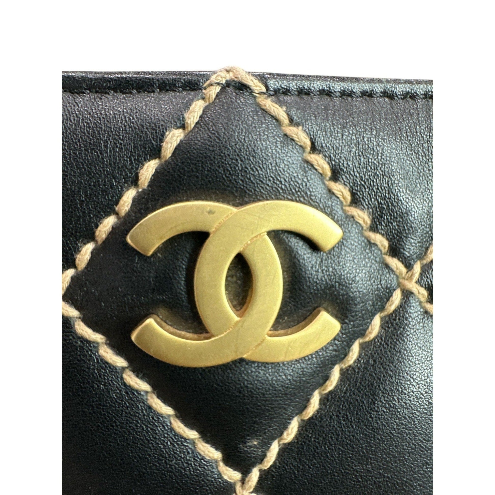 Close-up of a black leather product with gold stitching and Chanel logo.